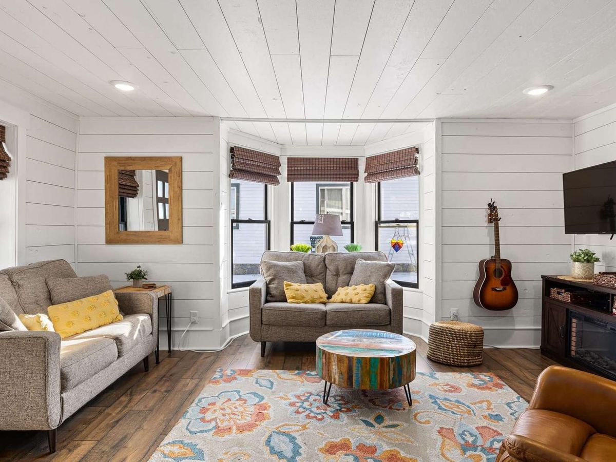 This bright and playful cabin brings charm with white shiplap walls, colorful accents, and a cozy setup perfect for slow mornings. Curl up on the couch, strum the guitar, or sip coffee under the bay window sunlight.