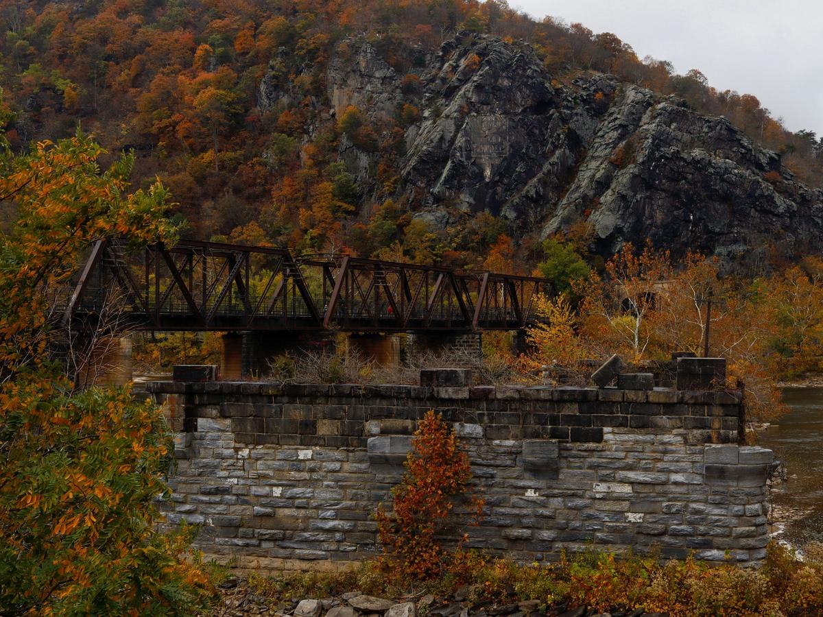 Bridge over stone wall with fall foliage surrounding the area and on the mountain