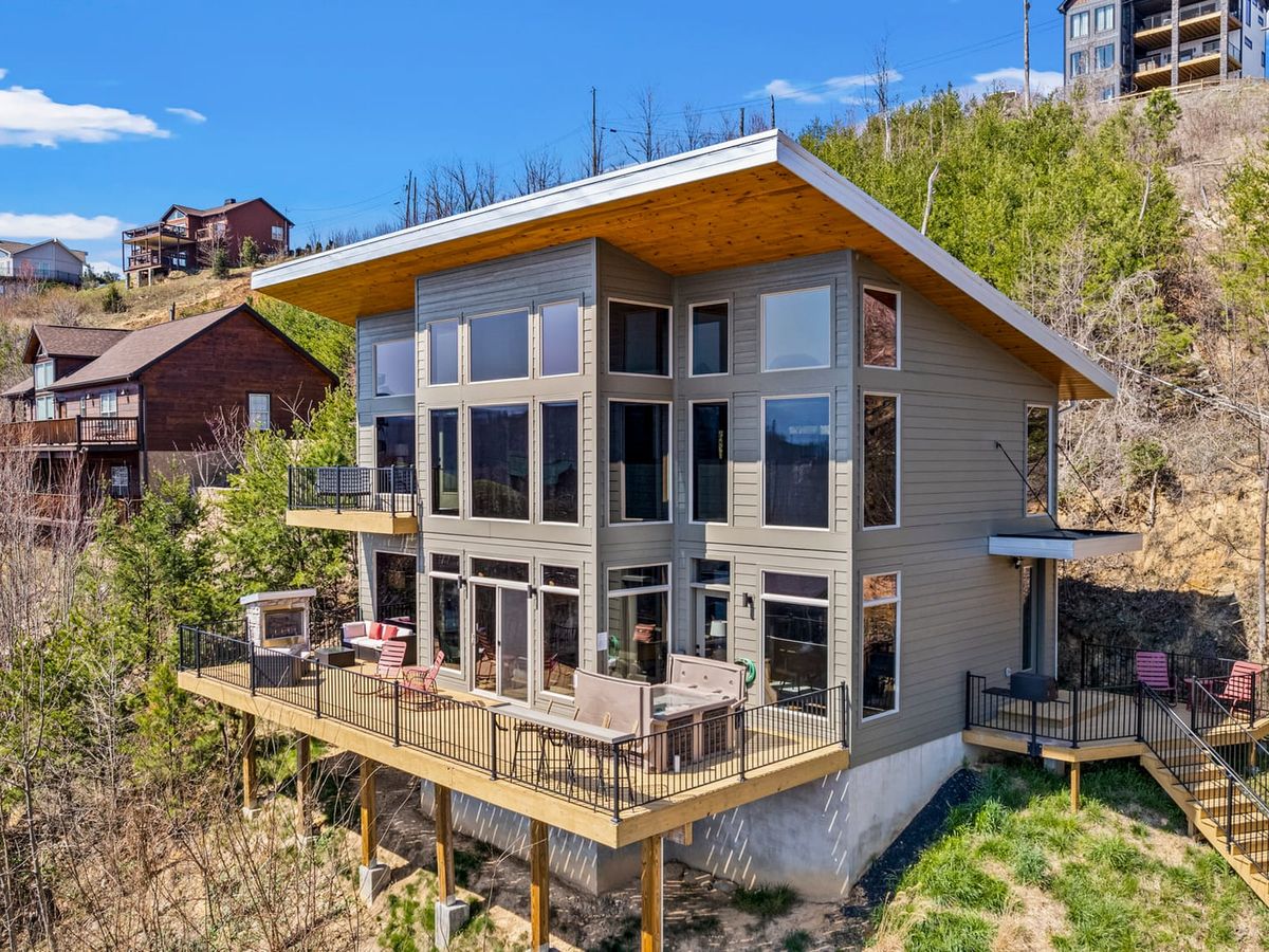 A modern mountain cabin in Gatlinburg, Tennessee, surrounded by wooded hills and panoramic views. Expansive windows and wraparound decks let guests soak in the natural beauty.