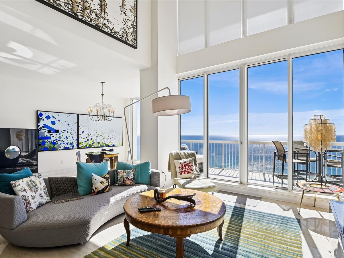 Interior of living room with grey couch and large open windows that overlook the ocean