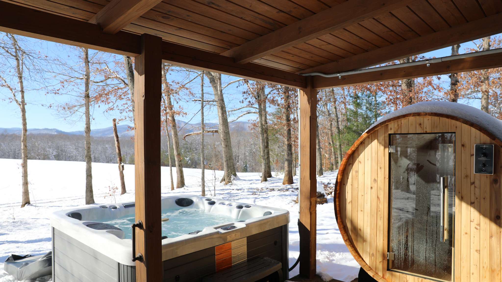Private hot tub and sauna side by side underneath balcony with snow in the background