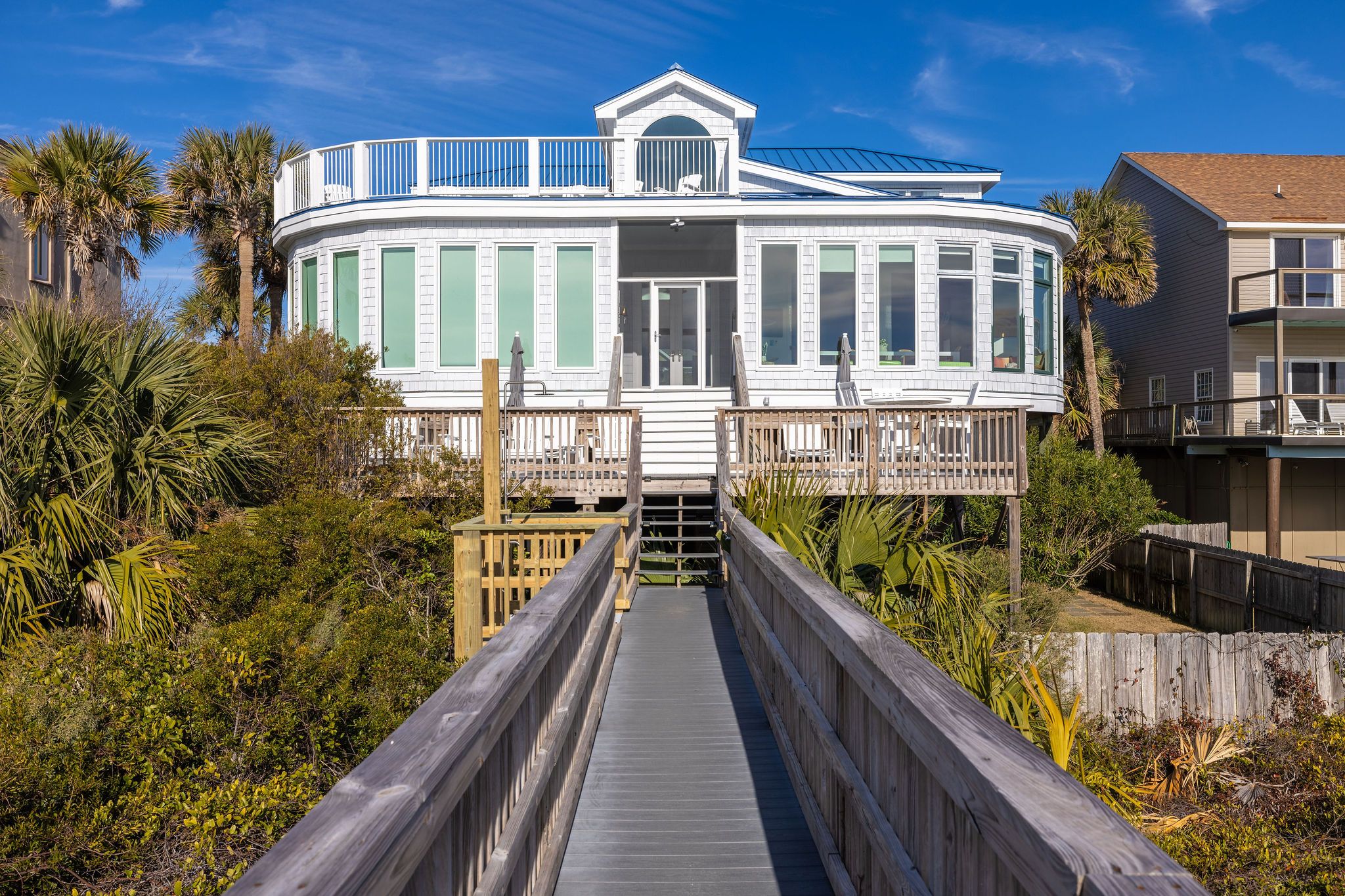Exterior of white vacation rental in Folly Beach with several open windows and deck leading to beach