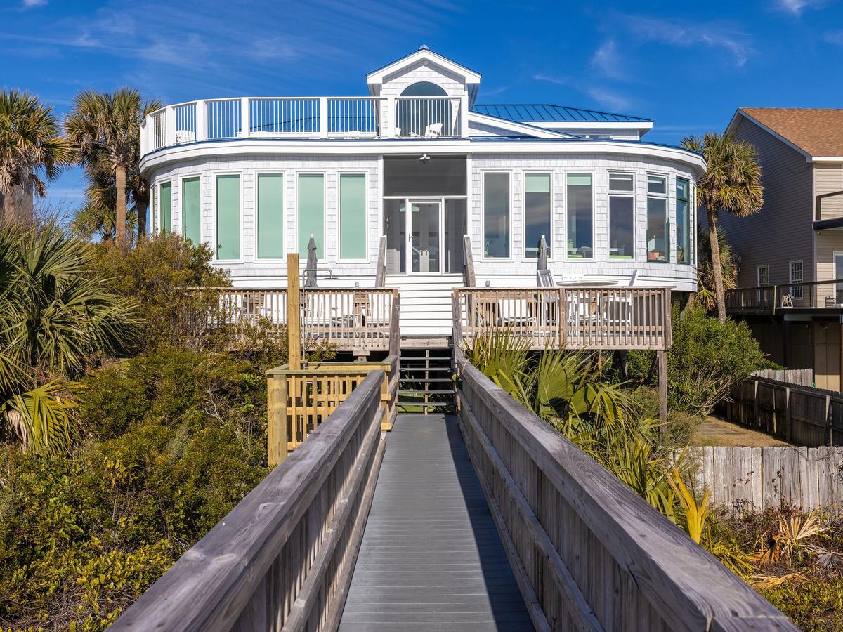 Exterior of white vacation rental in Folly Beach with several open windows and deck leading to beach