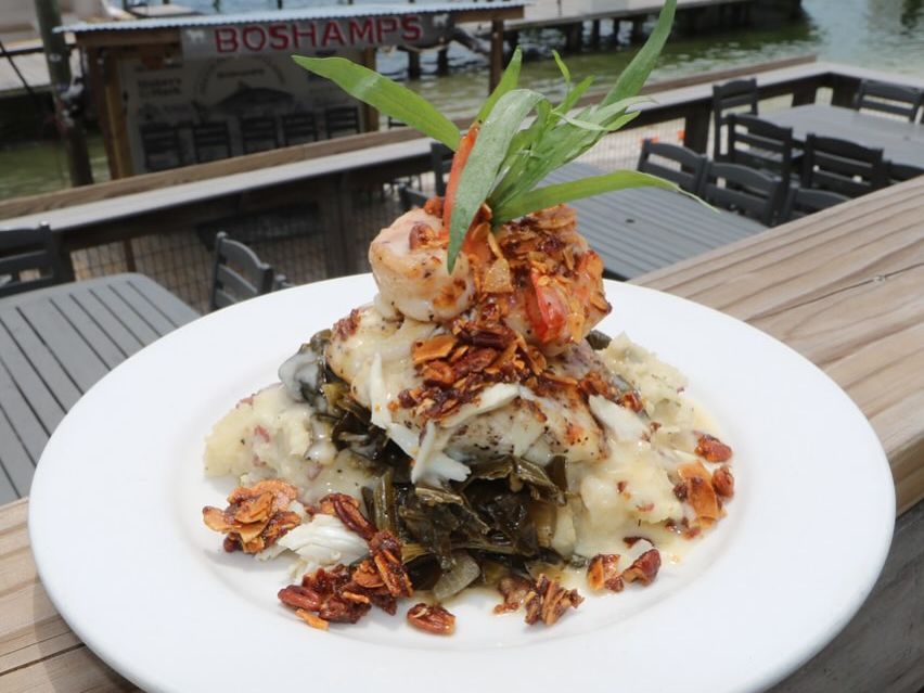 A stunning seafood tower at Boshamps, stacked with mashed potatoes, collard greens, grilled shrimp, and toasted pecans. Served dockside with views of the Destin Harbor.