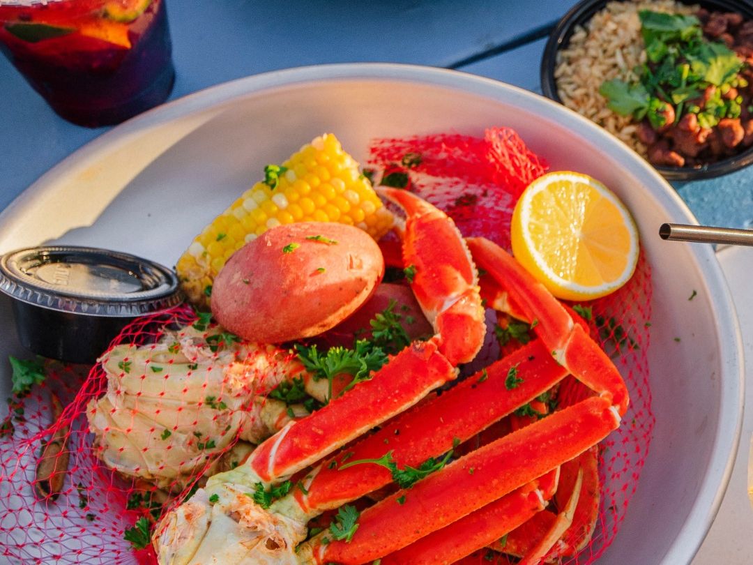 Fresh crab legs with corn, potatoes, and lemon in a bright seafood boil bowl. The perfect dinner for seafood lovers with refreshing drinks and salad on the side.