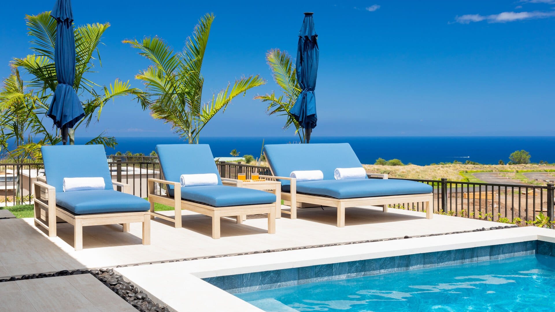 Three blue lounge chairs side by side with private pool in front and gate surrounding area