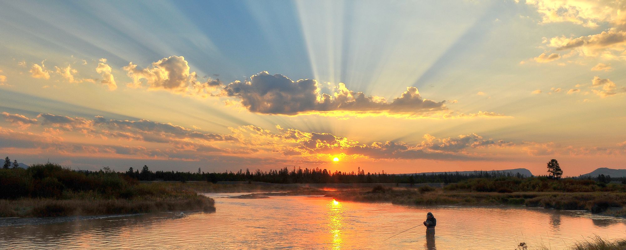 View of a Person Fly Fishing in a West Yellowstone River At Sunset