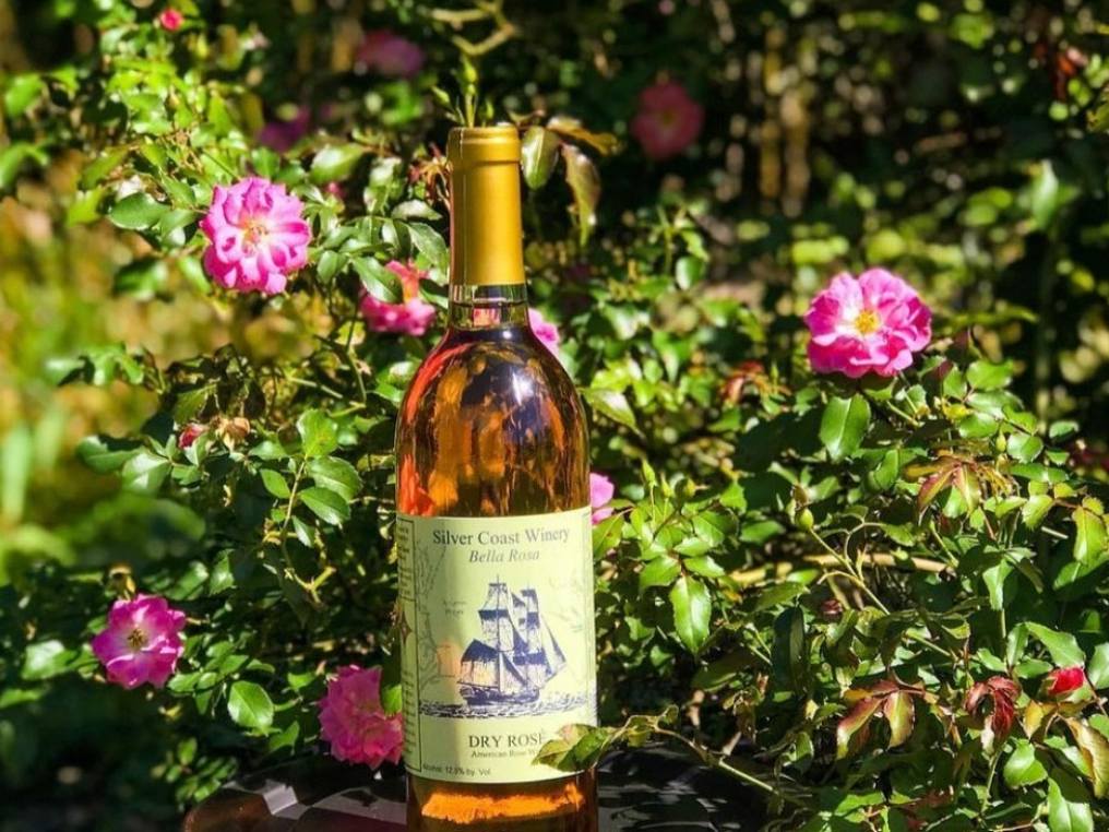 wine bottle on barrell with pink rose bush in the back