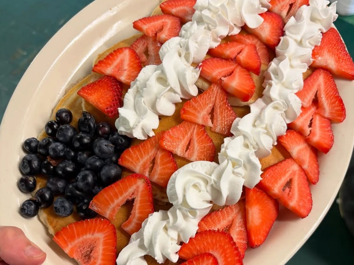 A plate of golden pancakes topped with fresh strawberries, blueberries, and swirls of whipped cream.