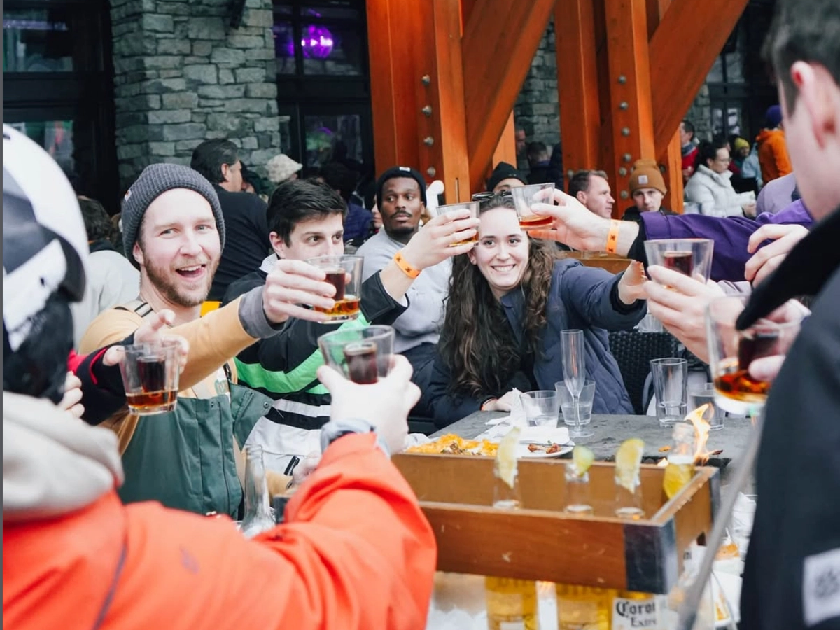 Group of friends gathered at an outdoor mountain bar, raising glasses in a celebratory toast amid a lively après-ski atmosphere.
