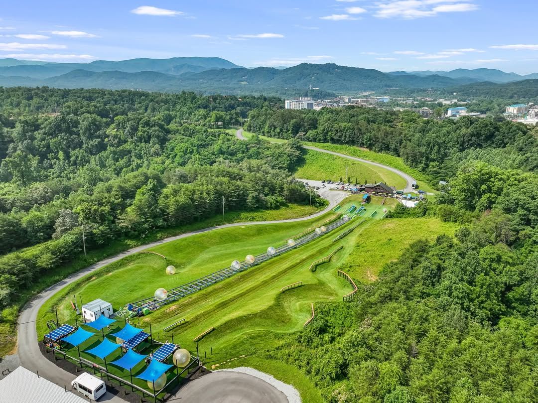 Aerial view of Outdoor Gravity Park in Pigeon Forge showing rolling green hills and giant zorb balls. The adventure park offers unique downhill rides with stunning Smoky Mountain scenery.