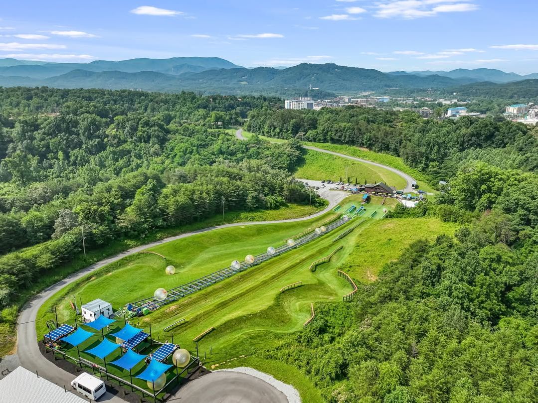Aerial view of Outdoor Gravity Park in Pigeon Forge showing rolling green hills and giant zorb balls. The adventure park offers unique downhill rides with stunning Smoky Mountain scenery.