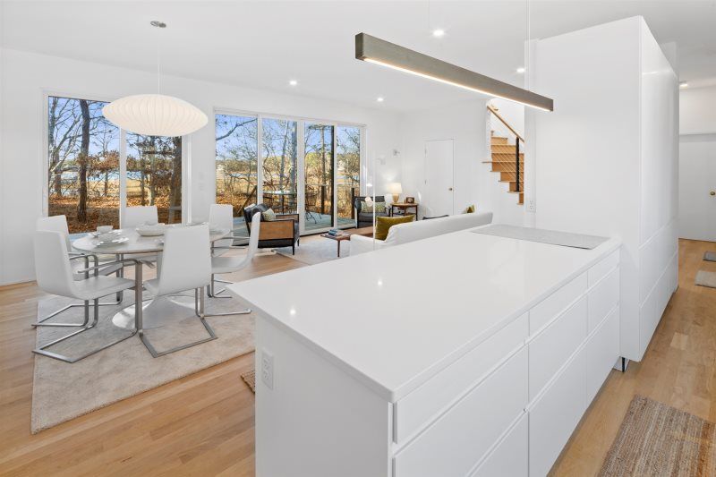 Sleek open-concept kitchen and dining area with crisp white cabinetry, a waterfall island, modern pendant lighting, floor-to-ceiling windows, and warm wood floors creating a bright, contemporary retreat.