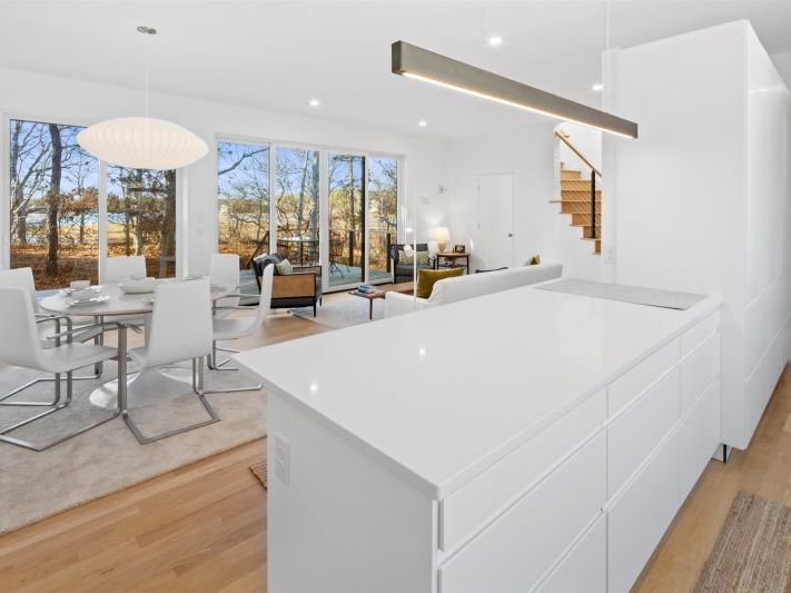 Sleek open-concept kitchen and dining area with crisp white cabinetry, a waterfall island, modern pendant lighting, floor-to-ceiling windows, and warm wood floors creating a bright, contemporary retreat.