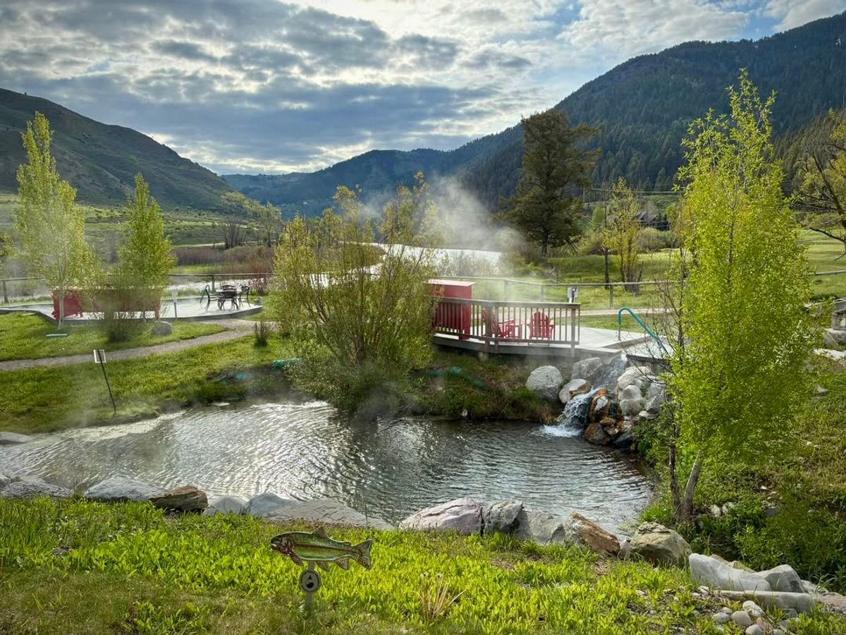team rises over natural pools at Astoria Hot Springs Park, framed by green trees and mountains. This peaceful retreat is a favorite spot for soaking and connecting with nature.