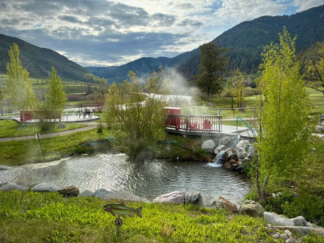 team rises over natural pools at Astoria Hot Springs Park, framed by green trees and mountains. This peaceful retreat is a favorite spot for soaking and connecting with nature.