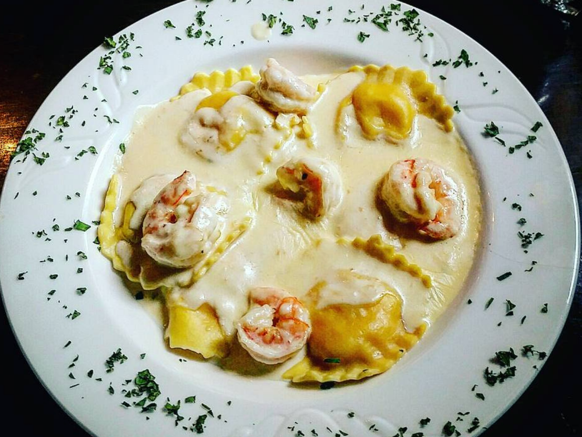 Plate of ravioli in a creamy white sauce topped with shrimp, garnished with parsley around the edges.