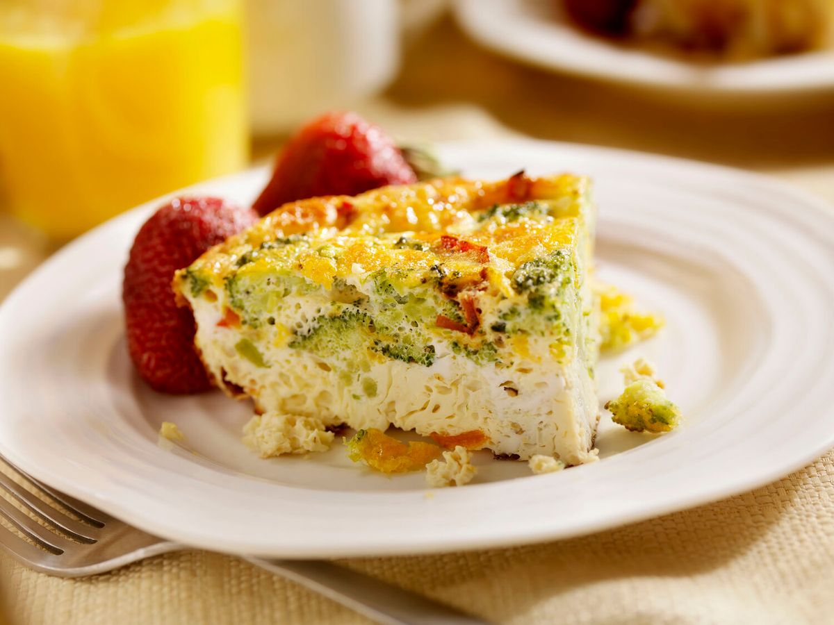 Close-up of a fresh veggie frittata served with strawberries on a white plate—Sunday breakfast done right. The colorful dish looks warm, homemade, and perfect to enjoy with morning sunshine.