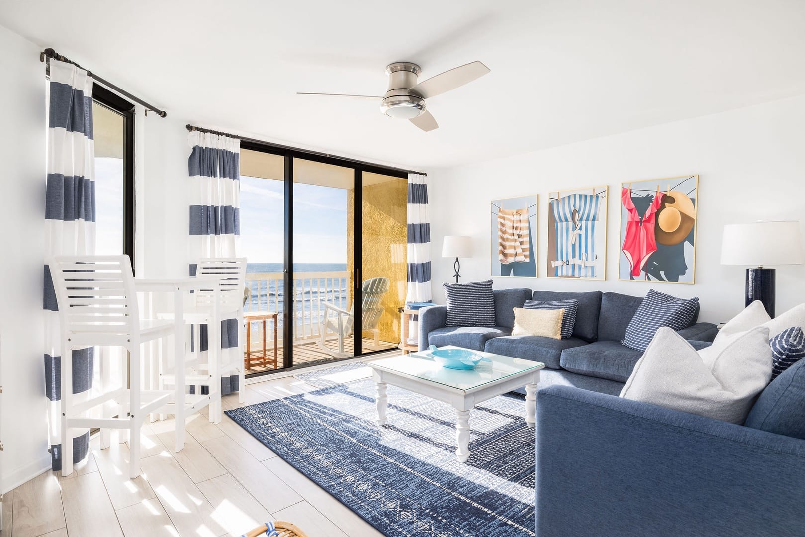 Coastal-style living room filled with natural light and direct access to an oceanfront balcony. Soft blue tones and comfortable seating create a relaxed space to unwind after a day on Folly Beach.