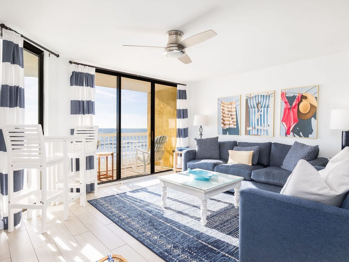 Coastal-style living room filled with natural light and direct access to an oceanfront balcony. Soft blue tones and comfortable seating create a relaxed space to unwind after a day on Folly Beach.