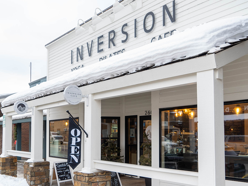 Snow rests on the roof of Inversion Yoga in Jackson, Wyoming, a cozy spot that blends yoga, Pilates, and a welcoming café for wellness seekers. The inviting exterior with its open sign shows it’s ready to welcome locals and visitors alike.