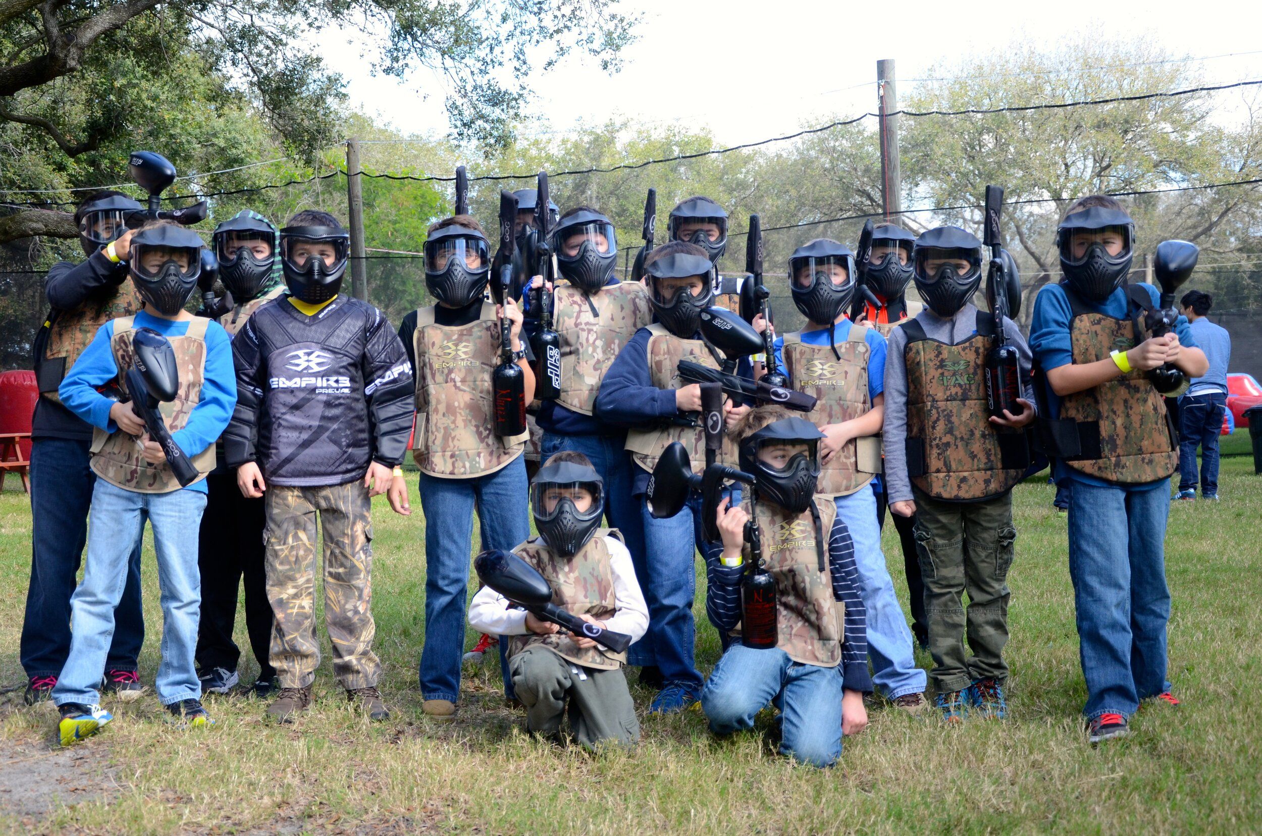 A group of kids geared up in helmets and camouflage vests prepare for an exciting paintball match at Outdoor Xtreme. The outdoor field is perfect for fun, teamwork, and adventure.