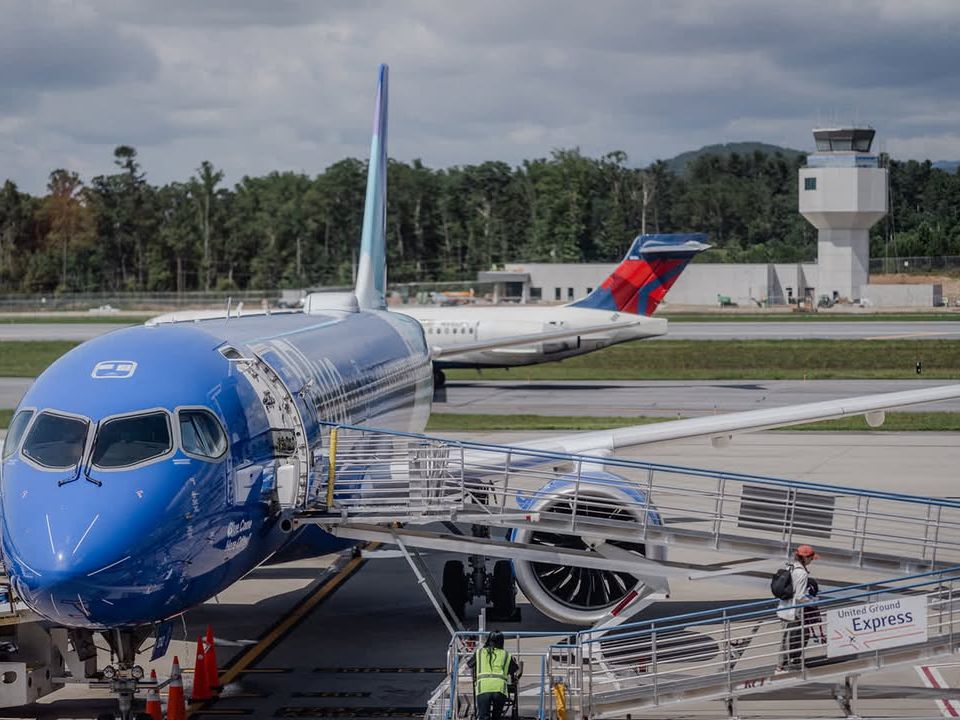 A blue jet prepares for boarding at Asheville Regional Airport, with mountains in the background. This airport makes traveling into Western North Carolina quick and convenient.