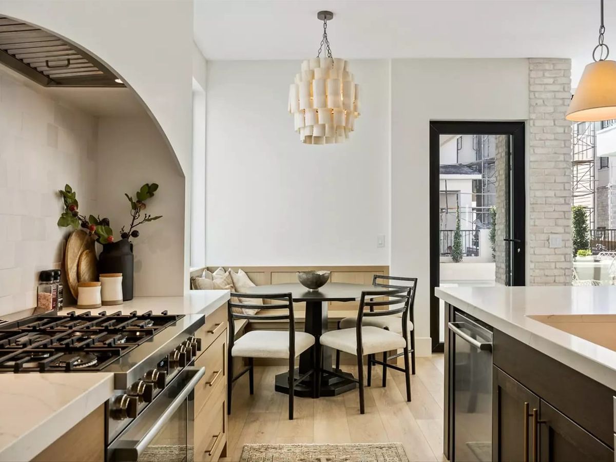 Cozy kitchen nook with a built-in bench, round dining table, and modern light fixture beside a bright, open cooking space.