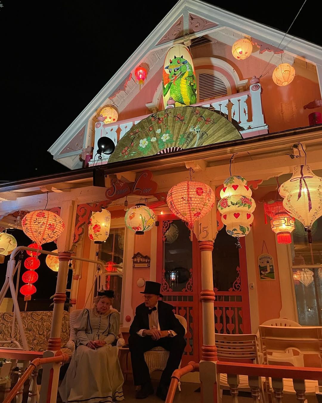 A pastel cottage in Oak Bluffs glows under a canopy of colorful paper lanterns during Grand Illumination Night. Dressed in period clothing, two people sit on the porch, capturing the nostalgic charm and magic of this beloved Martha’s Vineyard tradition.