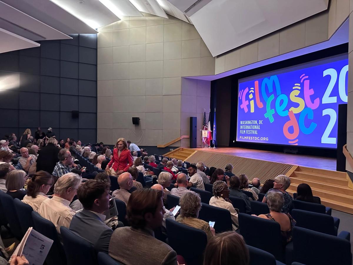 A full auditorium of film enthusiasts gathers for a screening at the Washington DC International Film Festival, with the colorful FilmFestDC logo displayed prominently on the large screen at the front of the modern theater. 