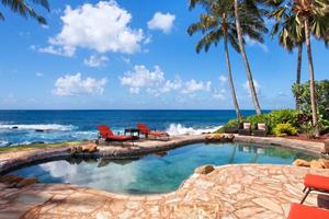 A tropical vacation rental with a private oceanfront pool and palm trees is paired with the headline “Airbnb Is Changing Its Fees on September 15.” The image introduces a travel guide explaining what Airbnb’s fee changes could mean for travelers planning their next vacation.