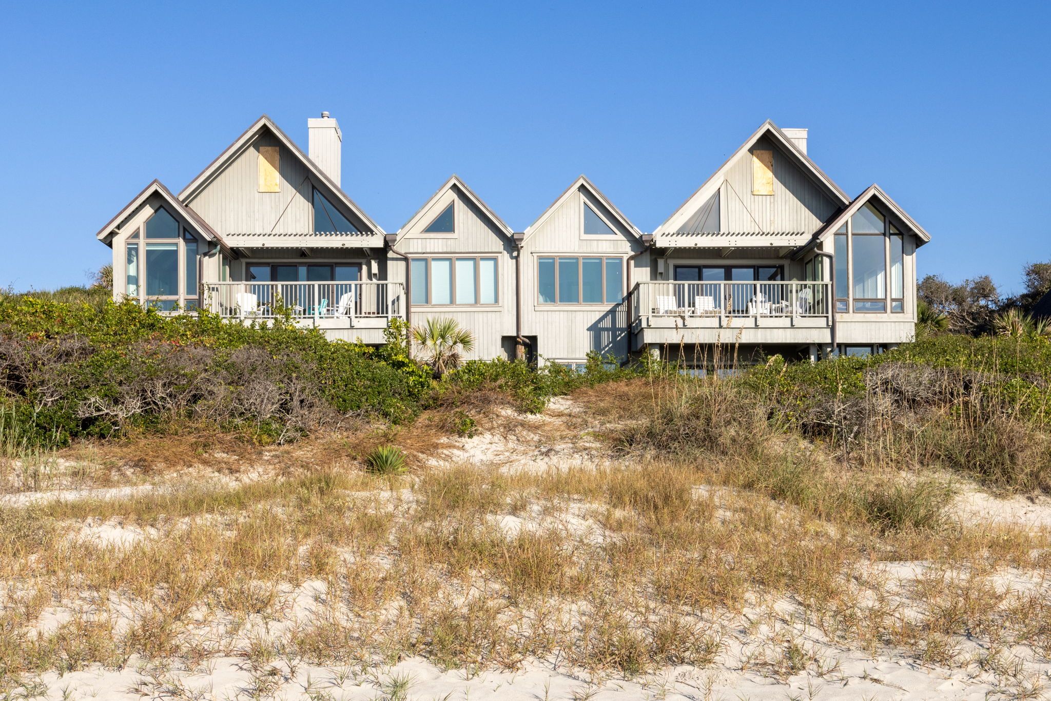 Sandy beach with gras in the sand and large house on the hill