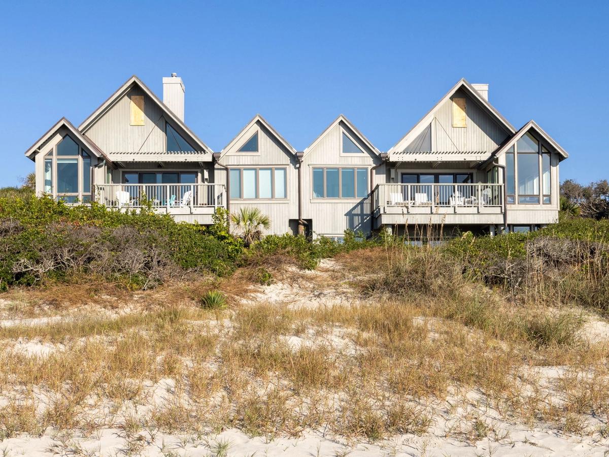 Sandy beach with gras in the sand and large house on the hill