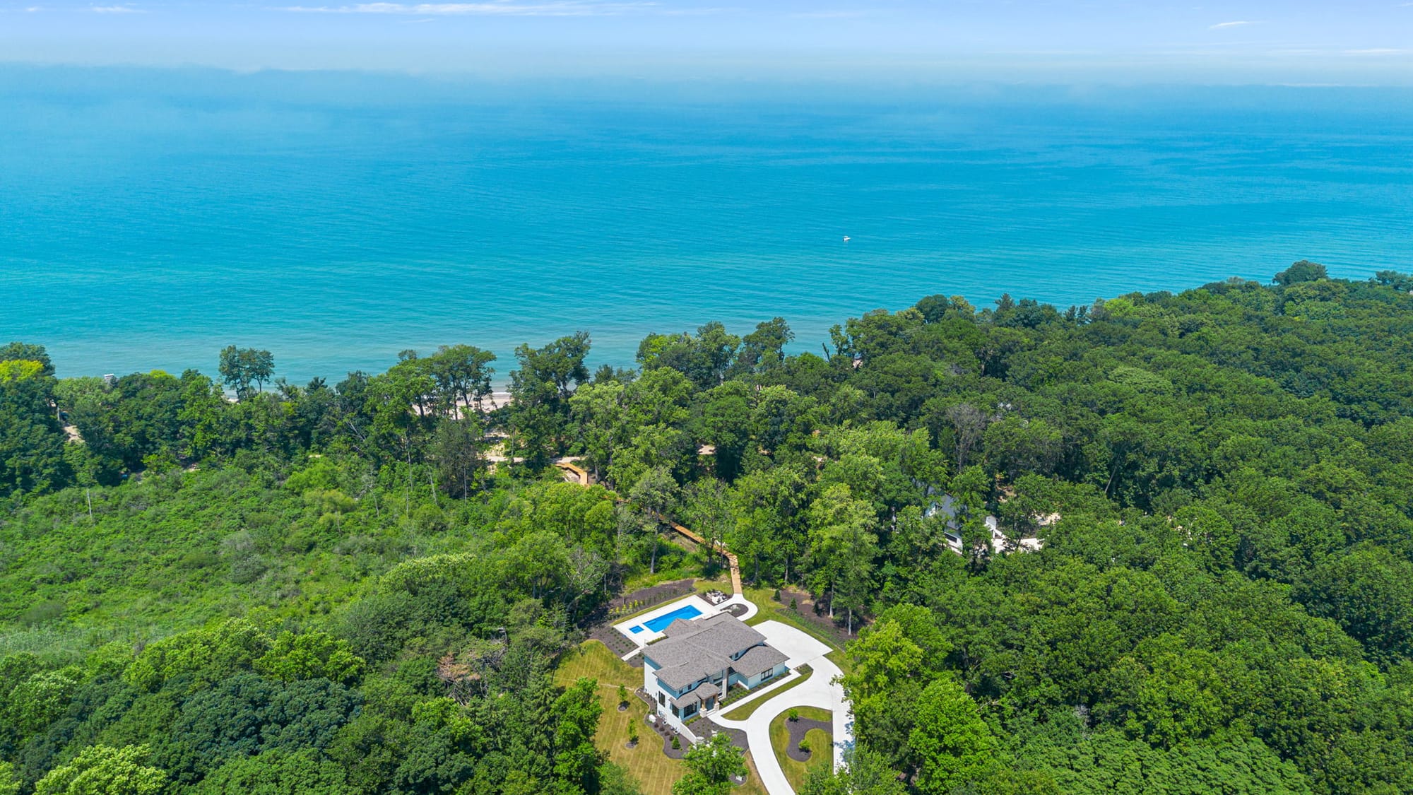 Aerial view of a secluded home surrounded by forest with a clear blue pool and sweeping views of the ocean. The scene reflects a peaceful escape where personalized itineraries help you explore both nature and luxury.
