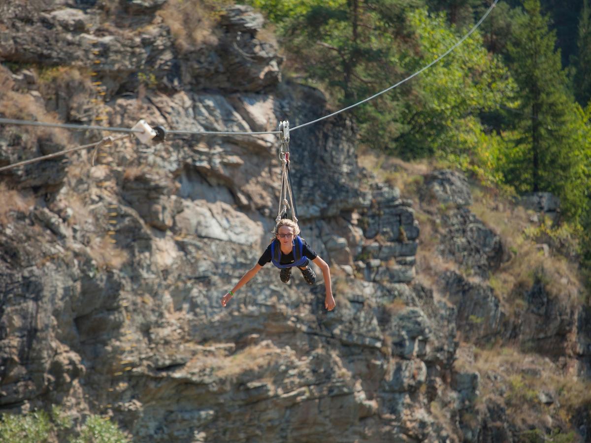 An adventurer soars across a canyon on a zipline surrounded by rugged cliffs and forest. Big Sky ziplining brings adrenaline and unforgettable mountain views.