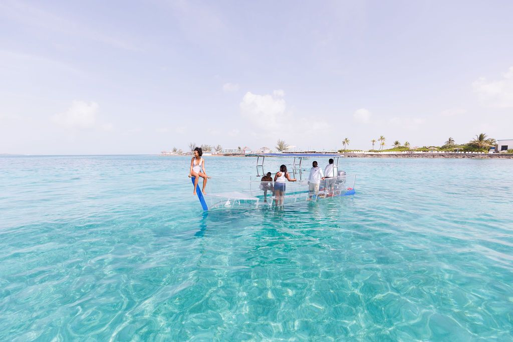 A group of friends enjoys a glass-bottom boat ride over crystal-clear turquoise waters, revealing the marine life below. It’s the perfect way to experience the Bahamas’ stunning underwater world without getting wet.