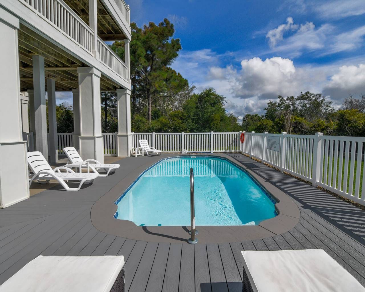 A private outdoor pool sits beneath a raised deck, surrounded by lounge chairs and a secure white fence. This peaceful mountain cabin pool area is perfect for relaxing after a day of hiking or sightseeing.
