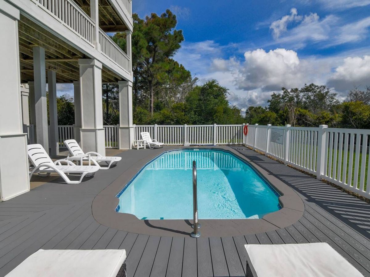 A private outdoor pool sits beneath a raised deck, surrounded by lounge chairs and a secure white fence. This peaceful mountain cabin pool area is perfect for relaxing after a day of hiking or sightseeing.