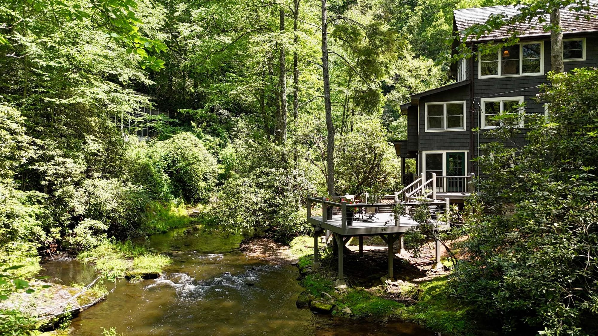 A modern covered patio with a cozy fireplace offers stylish outdoor seating surrounded by trees. The open-air design blends comfort with nature, creating a perfect mountain getaway space. It’s a great spot to relax by the fire and enjoy cool evenings in North Carolina.