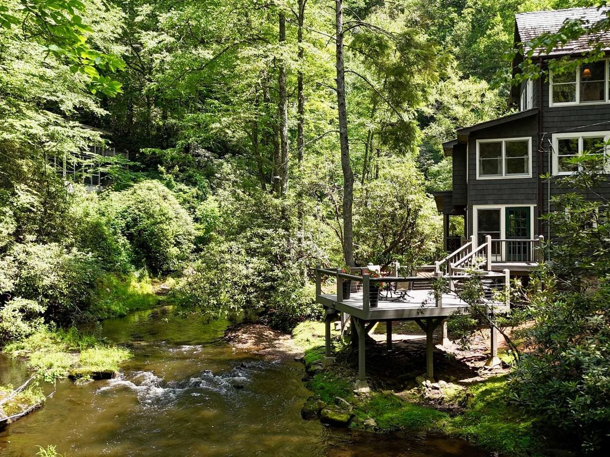 A modern covered patio with a cozy fireplace offers stylish outdoor seating surrounded by trees. The open-air design blends comfort with nature, creating a perfect mountain getaway space. It’s a great spot to relax by the fire and enjoy cool evenings in North Carolina.