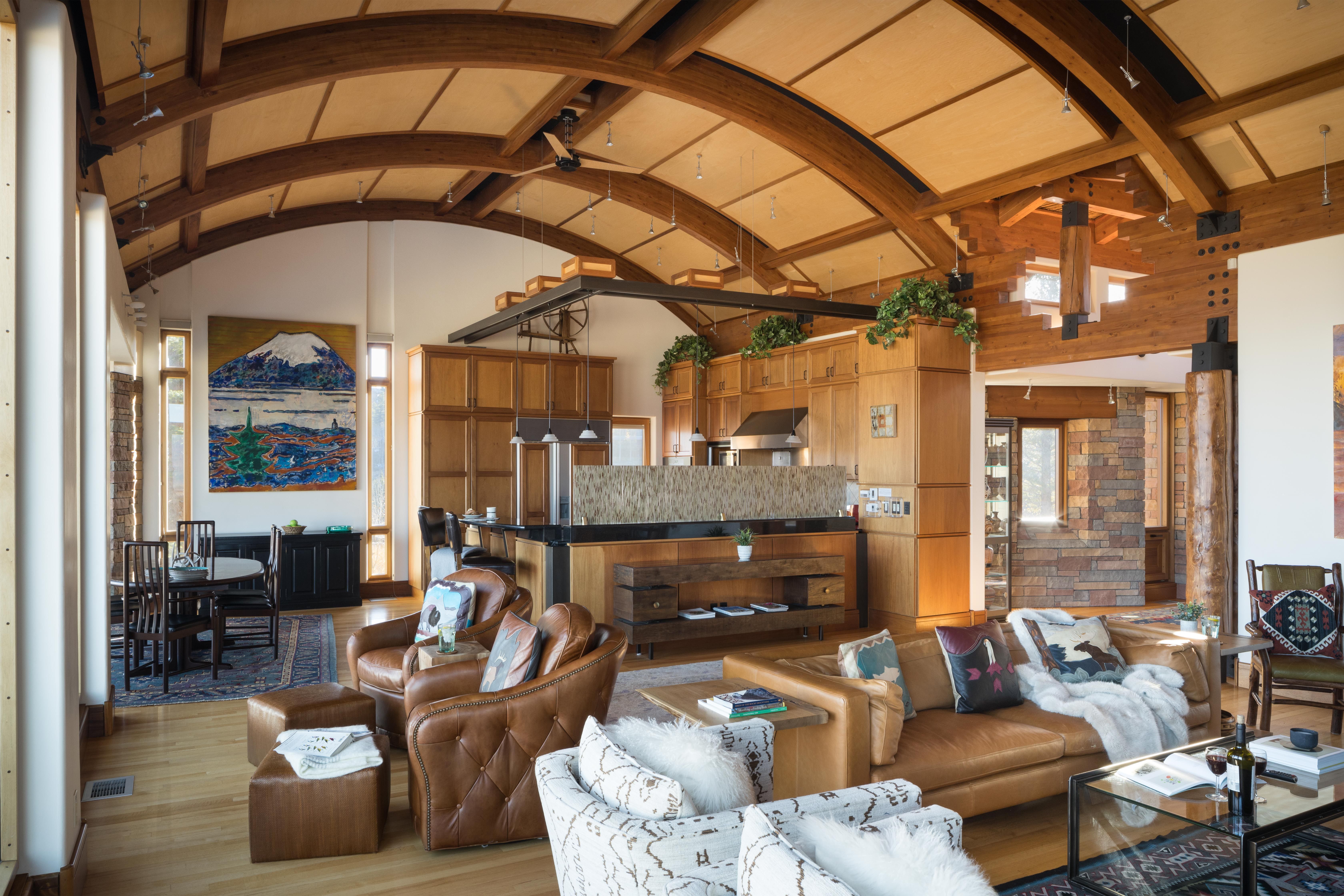 Stylish mountain home interior with vaulted wood-beam ceilings, an open-concept kitchen, cozy leather seating, and eclectic decor featuring bold artwork and natural light.