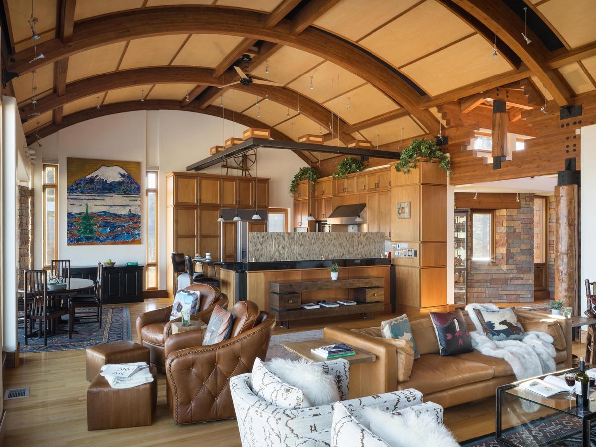 Stylish mountain home interior with vaulted wood-beam ceilings, an open-concept kitchen, cozy leather seating, and eclectic decor featuring bold artwork and natural light.