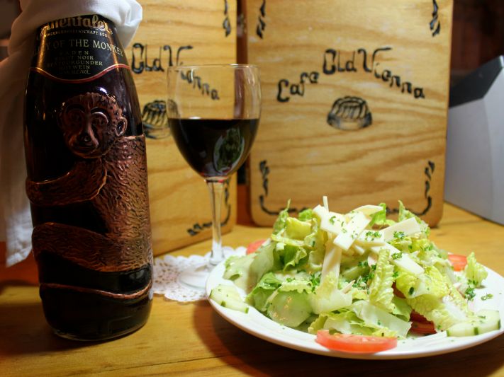 A fresh green salad with cucumbers, tomatoes, and cheese served with a glass of red wine. Cafe Old Vienna is known for bringing authentic Austrian and German flavors to Myrtle Beach.