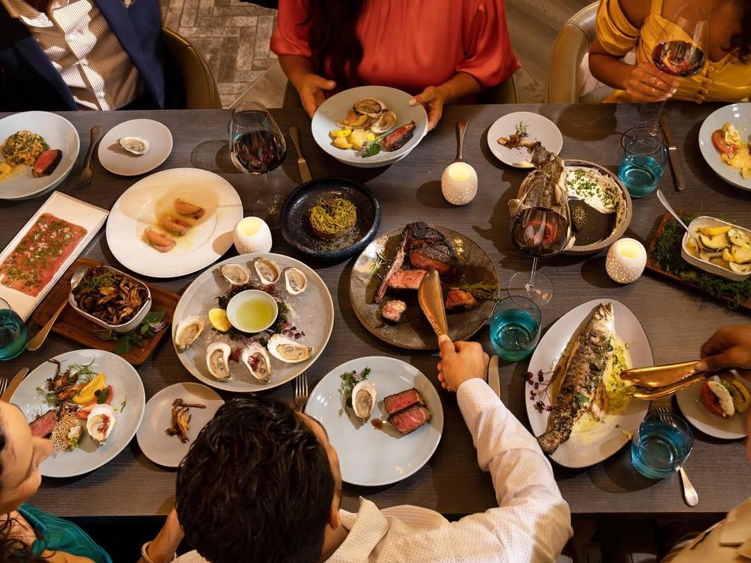 Guests enjoying a feast at Knife & Spoon with oysters, steak, whole grilled fish, and fine wine. A luxury dining experience perfect for celebrations.