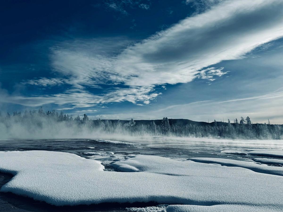 Ice and snow on land wihth water surrounding it and trees in the background with mistin between trees