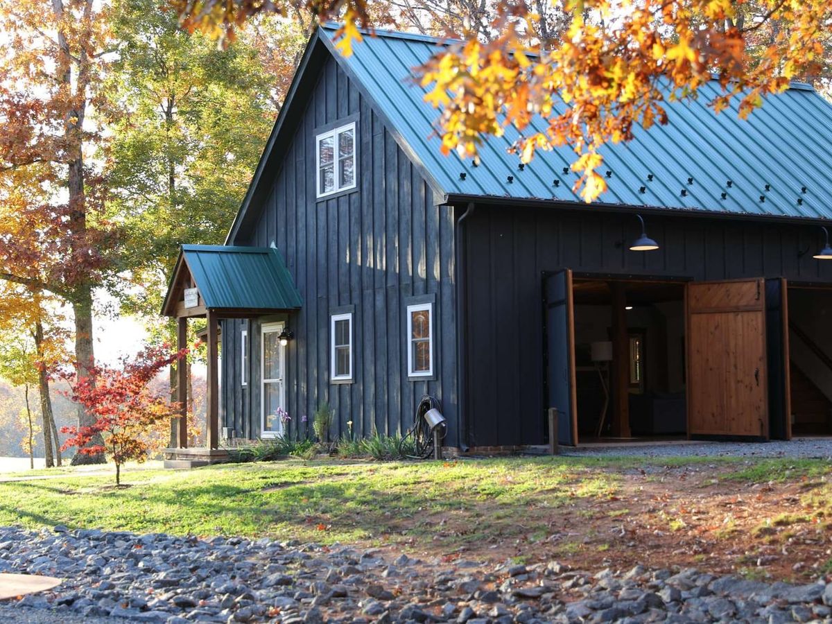 A grand brick estate with multiple dormer windows and traditional green shutters stands surrounded by tall trees. Its wide front yard and symmetrical design give it a stately, historic feel perfect for large group stays.