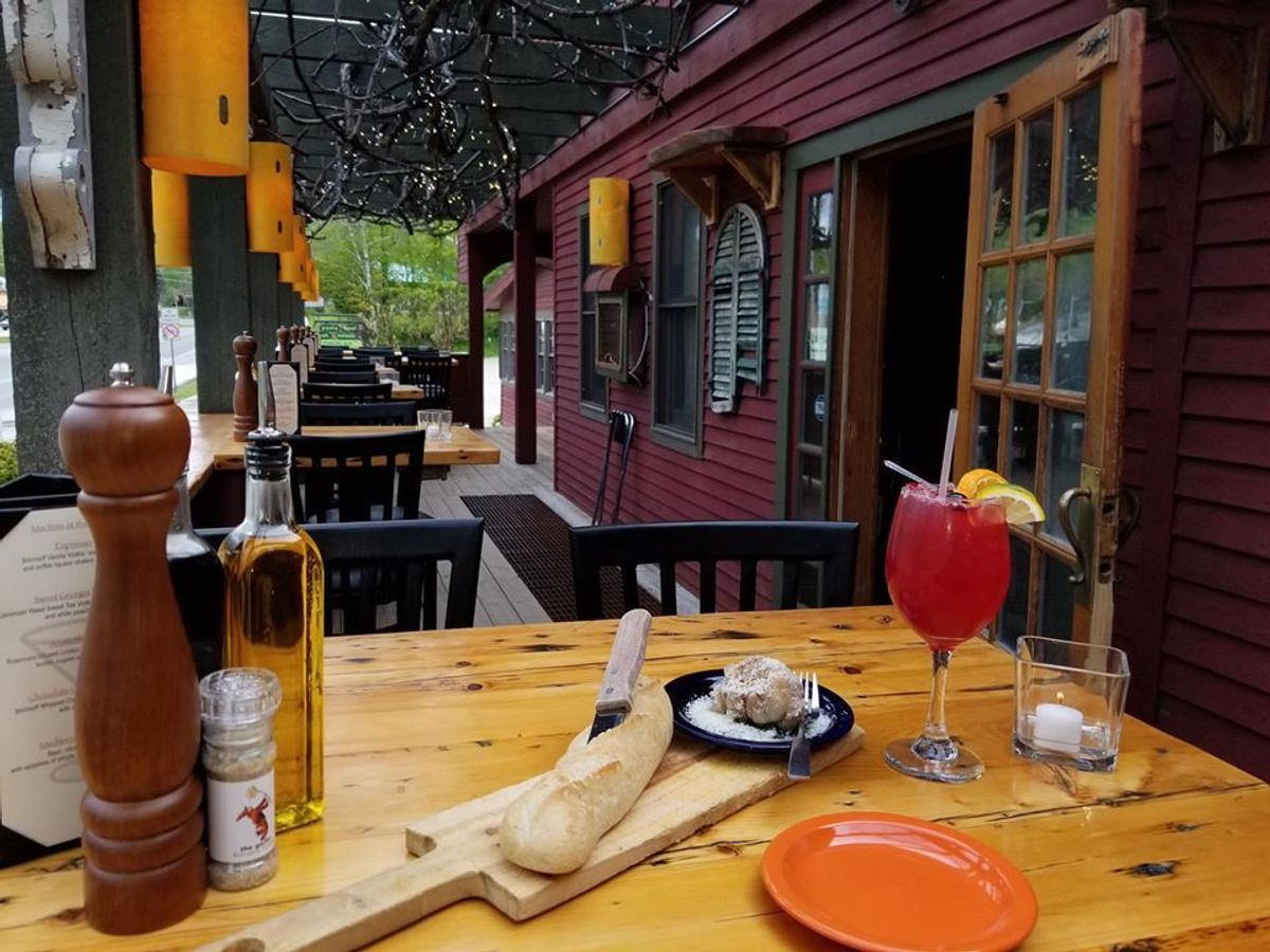 Outdoor dining table at The Garlic restaurant featuring fresh bread, olive oil, and a bright red cocktail. The cozy patio setting with wooden tables and soft lighting creates a charming Italian dining atmosphere. This popular restaurant is known for its flavorful dishes and welcoming ambiance.