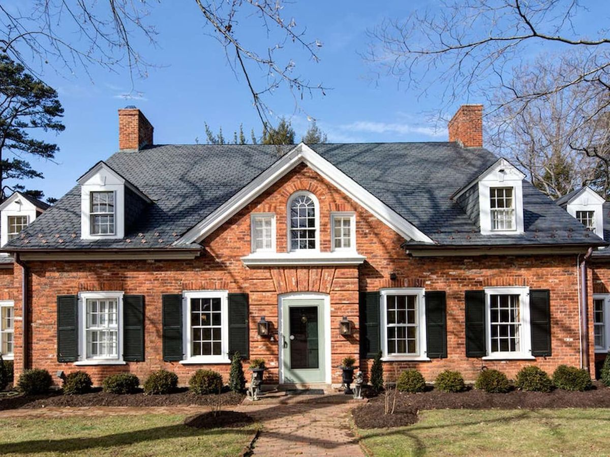 A classic red-brick colonial home with white trim and a gabled roof sits on a well-manicured lawn. This timeless home offers old-world charm with modern comfort for families and groups.