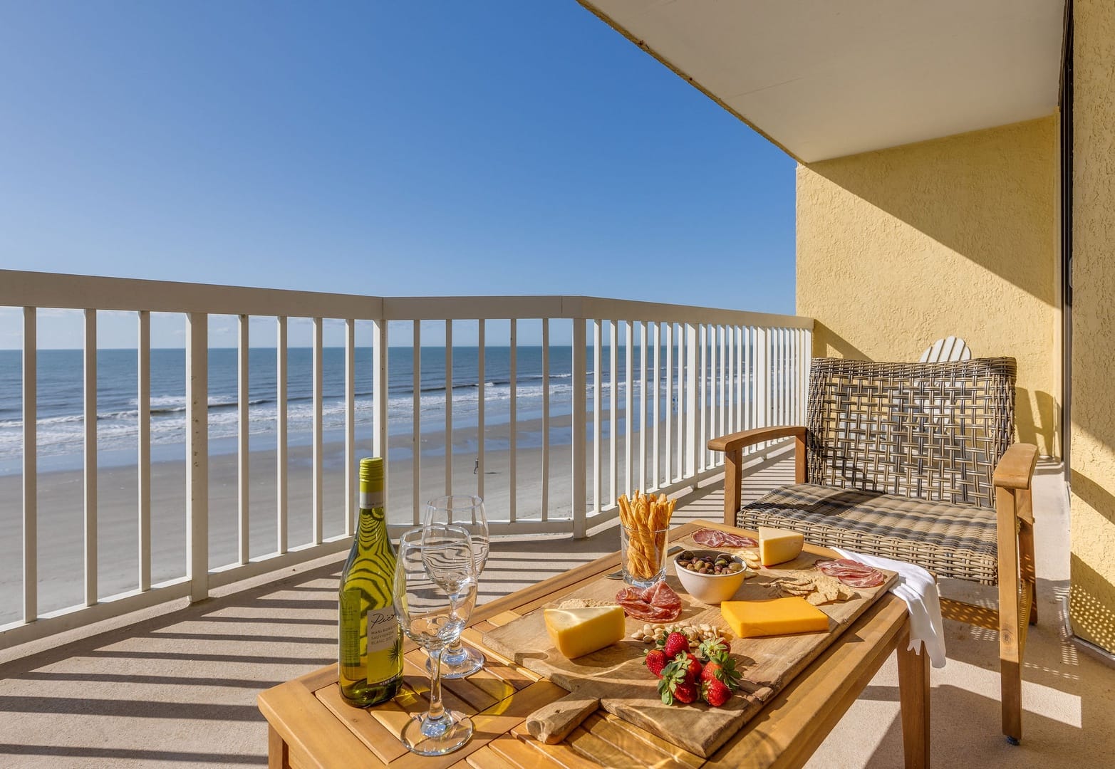 Private oceanfront balcony with lounge seating, wine glasses, and a snack board overlooking the shoreline. It’s an easy place to slow down, enjoy the sea breeze, and watch the waves roll in at Folly Beach.