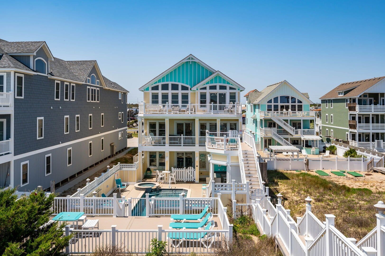 Bright blue vacation home with stairs going down and leading to private pool area with lounge chairs